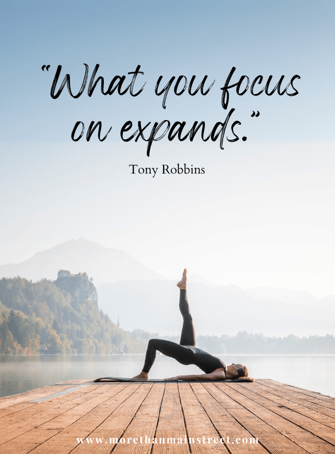 Woman doing yoga on a dock with mountain background with Tony Robbins quote "What you focus on expands"